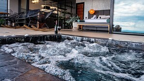 Een wellnessruimte met een bubbelbad, een zithoek en een slaapkamer met een groot raam.