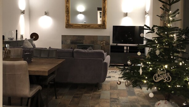 Ett mysigt vardagsrum med ett träpanelat tak, en öppen spis, en tv och en vackert dekorerad julgran.