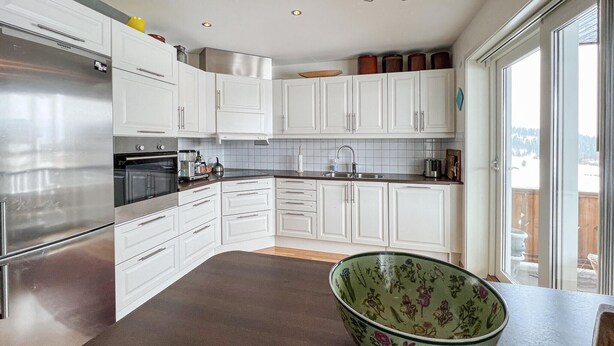 A modern kitchen with white cabinets, stainless steel appliances, and a large window providing a view of the outdoors. - 3 bedroom cozy apartment in Gålå (Gålå)