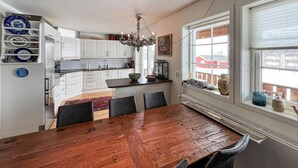 A modern kitchen with white cabinets, a wooden dining table, and a large window with a view of a red building. - 3 bedroom cozy apartment in Gålå (Gålå)