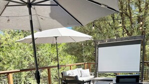 Terraza exterior con mesa, sillas, sofá y pantalla de proyector.