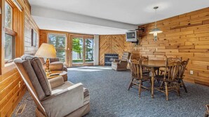 A cozy room with a fireplace, a television, a dining table with chairs, and a sofa. - Lakeside Condo #17 3BR 3BA Timberlane Resort (Park Rapids)