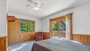 A bedroom with a bed, a chair, a ceiling fan, and a balcony with a view of trees. - Lakeside Condo #17 3BR 3BA Timberlane Resort (Park Rapids)