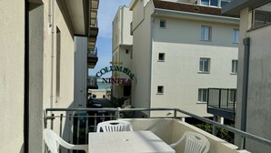A balcony with a table and chairs, overlooking a street with buildings. - Villa Bianca 6 - Carraro Immobiliare Jesolo (Lido di Jesolo)