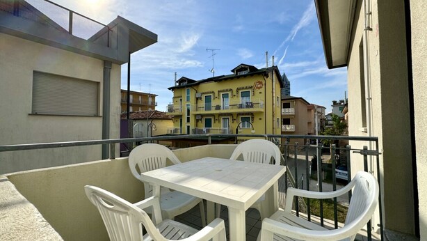 A balcony with a table and chairs, overlooking a yellow building with balconies.