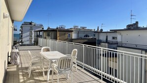 A balcony with a table and chairs, a white railing, and a view of neighboring buildings.