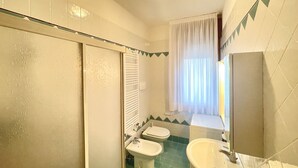 A bathroom with a shower, two toilets, a bidet, and a sink.