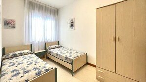 Un dormitorio con dos camas individuales, un armario y una ventana con cortinas.