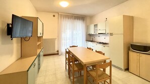 Una cocina funcional con mesa, sillas, televisor montado en la pared y microondas en la encimera.