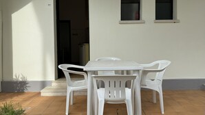 Taula blanca i quatre cadirees blanques davant d'un edifici amb un paviment de rajoles i un petit escaló que condueix a l'entrada.