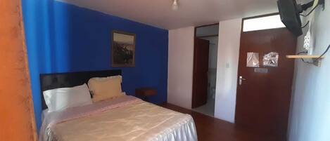 Un dormitorio con cama, mesita de noche, aire acondicionado de pared y puerta que da a otra habitación.