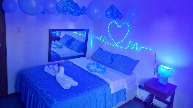 A bedroom with a bed, a nightstand, a neon heart decoration, and balloons on the wall. - Hotel Mi Secreto (Arequipa)