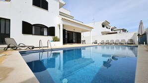 A swimming pool with lounge chairs and a building with a white facade and black shutters.