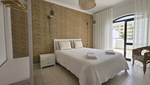 A hotel room with a large bed, a nightstand, a lamp, and a view of the outside.