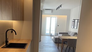 A modern kitchen with a wooden countertop, black faucet, and built-in appliances. There is a dining area with a table and chairs, and a living space with a sofa and a TV. - Athens City Chic apartment  in Petralona,with 2 double bedrooms and 2 bathrooms (Athens)