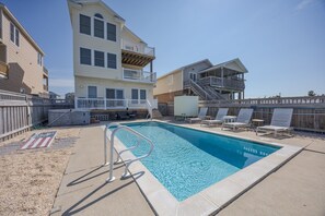 Une piscine avec un escalier en métal, entourée d’une terrasse en bois et de chaises longues.