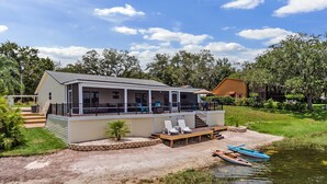 A house with a covered deck, outdoor seating, and a small boat by the water.