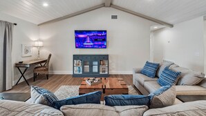 A living room with a high ceiling, a wooden coffee table, a sofa, a TV mounted on the wall, and a cabinet with glass doors.