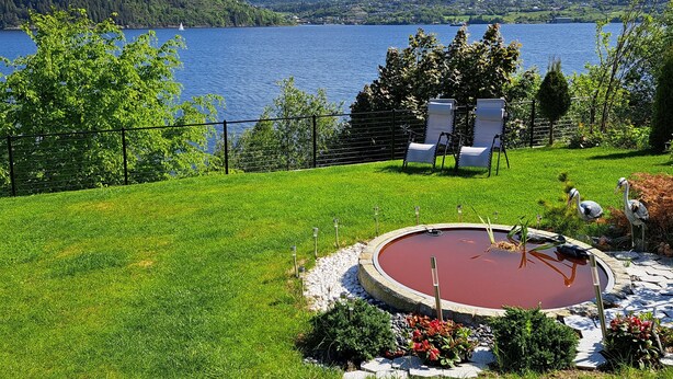 A backyard with a circular hot tub, a grassy lawn, and a view of a lake and mountains.