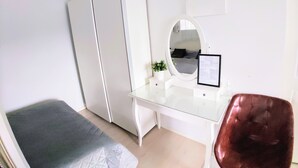 A bedroom with a bed, a desk, a chair, a mirror, and a wardrobe.