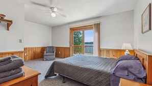 A bedroom with a bed, a chair, a wooden desk, a lamp, and a view of the outdoors. - Lakeside Condo #15 4BR 3BA Timberlane Resort (Park Rapids)