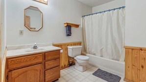 A bathroom with a wooden vanity, a toilet, a bathtub, a shower curtain, and a mirror with lights. - Lakeside Condo #15 4BR 3BA Timberlane Resort (Park Rapids)