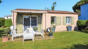 Une maison dotée d’un patio avec des chaises et une table blanches, le tout entouré d’une pelouse bien entretenue.