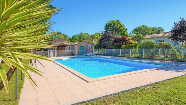 Une piscine rectangulaire bordée d’une terrasse carrelée, entourée d’une clôture blanche et d’une végétation luxuriante.