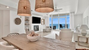 A spacious living room with a large wooden dining table, white sofas, and a view of the ocean through large windows.