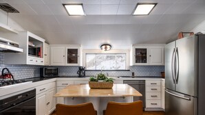 Une cuisine moderne avec des meubles blancs, un îlot central, deux chaises marron, des appareils en acier inoxydable et une fenêtre offrant une belle vue.