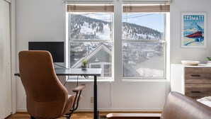 Une pièce comprenant un bureau, deux chaises, un téléviseur et une fenêtre donnant sur un paysage enneigé.