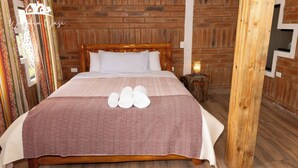 Ein hölzernes Bettgestell mit einem gemusterten Bettüberwurf, einem weißen Kopfkissen und vier zusammengerollten Handtüchern auf dem Bett.