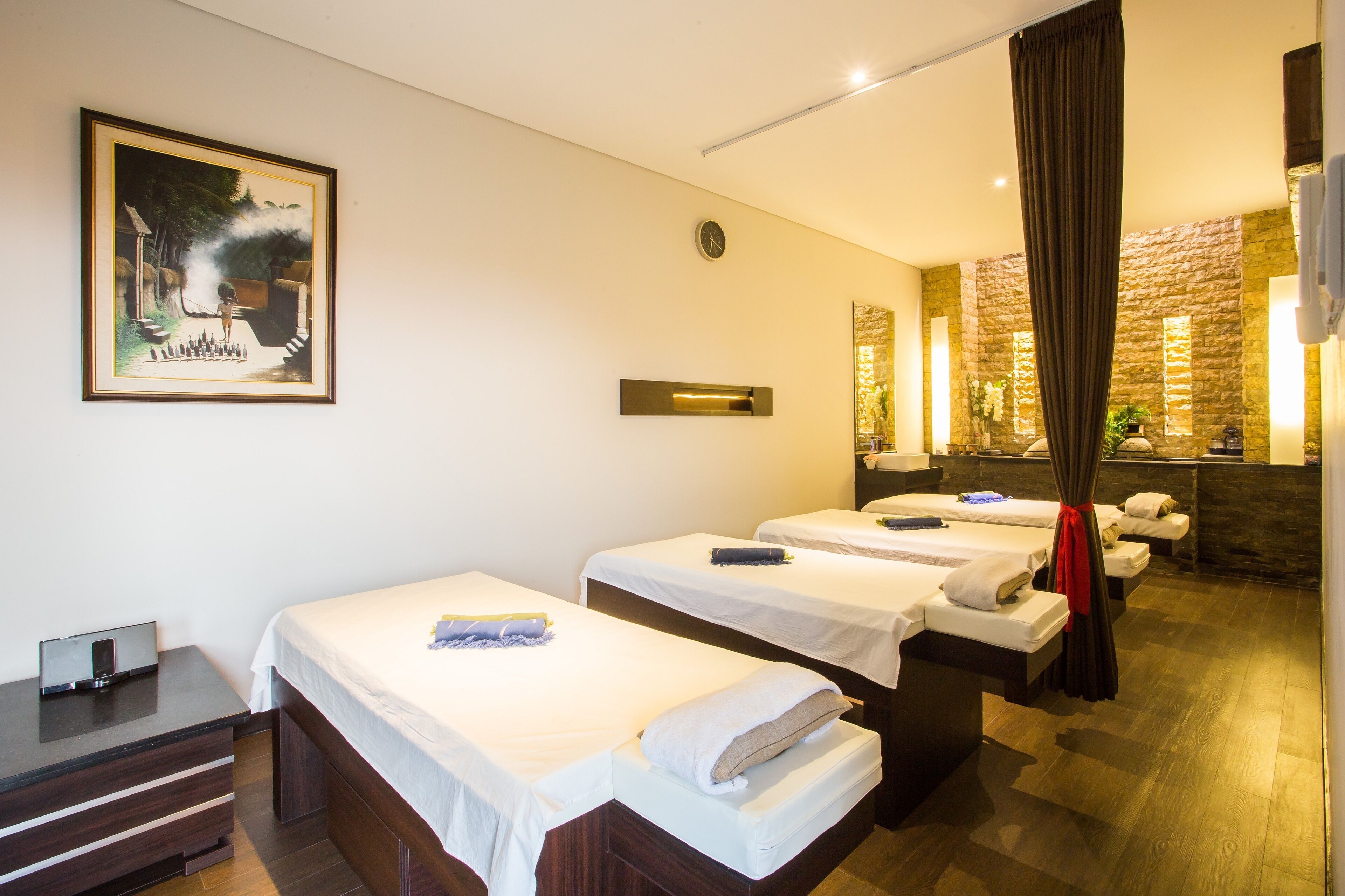 Une chambre d’hôtel avec deux lits simples, un petit bureau avec un miroir, une horloge et un tableau encadré au mur.