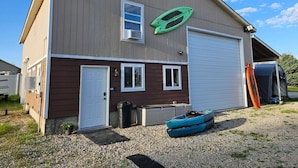 A two-story building with a garage door, a small attached shed, and a kayak in front. - Private Cabin, Breakfast, Dbl Tub, 75`TV, Kayak, WD, BBQ (West Point)