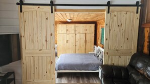Een slaapkamer met een bed, houten wanden, een plafondventilator en een zwarte leren fauteuil.