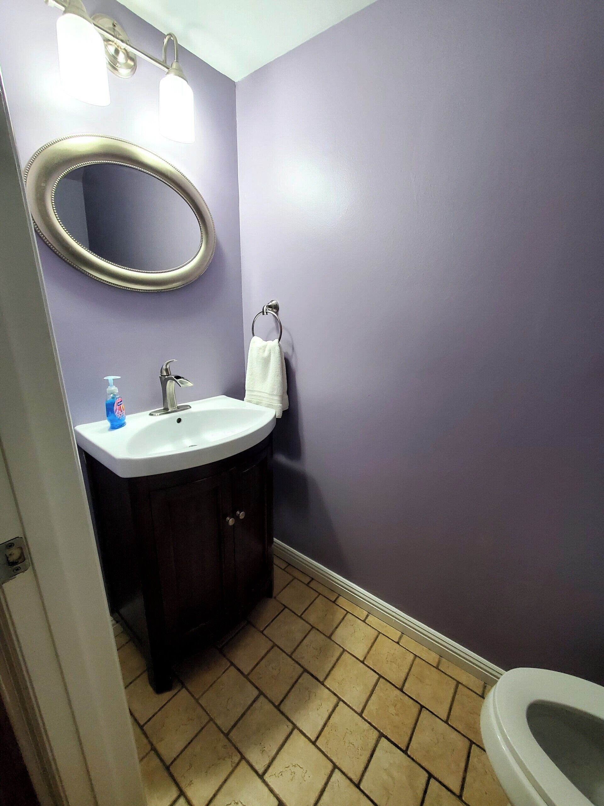 A bathroom with a white sink, dark wooden cabinets, a white towel, and a purple wall.