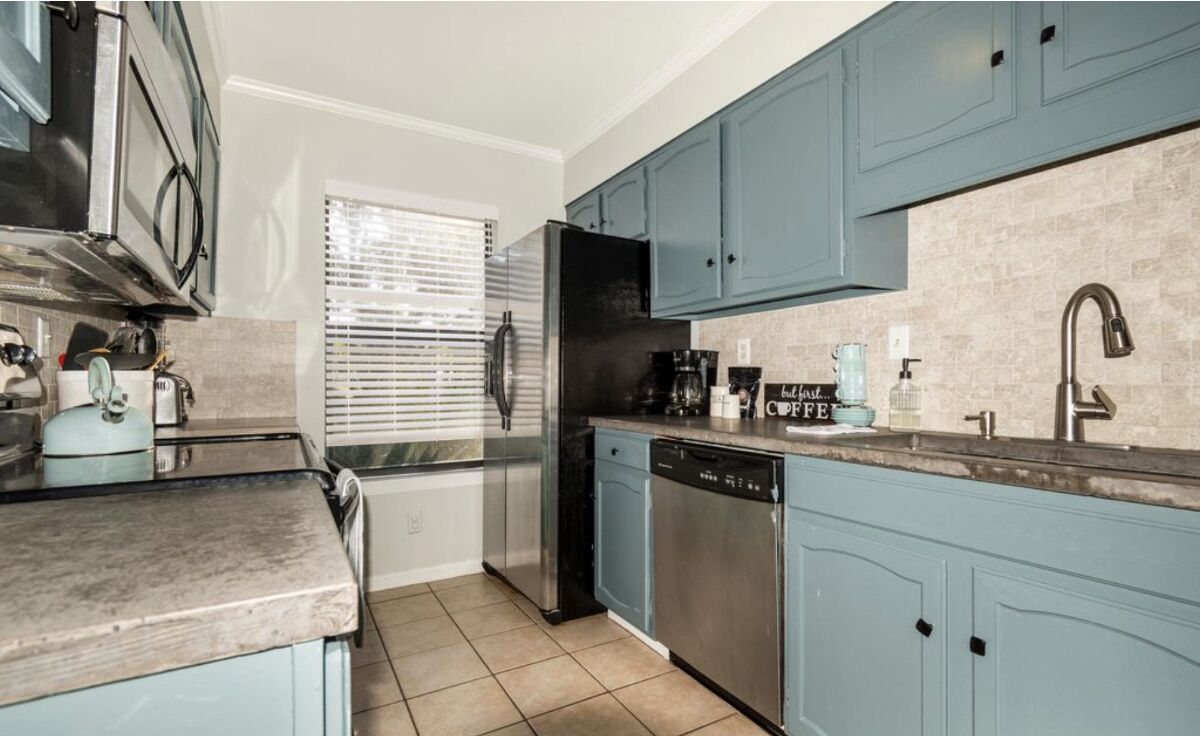 A compact kitchen with teal cabinets, stainless steel appliances, and a tiled backsplash.