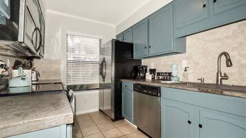 A compact kitchen with teal cabinets, stainless steel appliances, and a tiled backsplash.