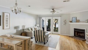 Un salon spacieux avec une cheminée, un fauteuil à rayures, une table à manger et un lustre.