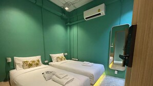 A hotel room with two beds, each with white linens and palm tree pillows. There is a mirror on the wall, an air conditioning unit above the beds, and a wooden door.