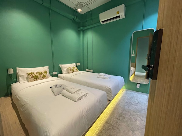 A hotel room with two beds, each with white linens and palm tree pillows. There is a mirror on the wall, an air conditioning unit above the beds, and a wooden door.
