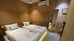 A hotel room with two beds, a mirror, an air conditioning unit, and a door with a handle.