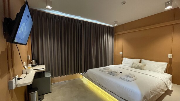 A modern hotel room with a large bed, a desk with a computer, a TV mounted on the wall, and a window with curtains.