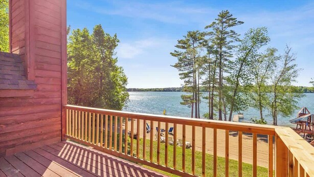 A wooden deck with a railing, overlooking a lake with trees and a dock. - Lakeside Condo #14 3BR 3BA Timberlane Resort (Park Rapids)