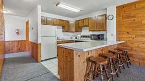 A kitchen with wooden cabinets, a central island with stools, a refrigerator, and a clock on the wall. - Lakeside Condo #14 3BR 3BA Timberlane Resort (Park Rapids)