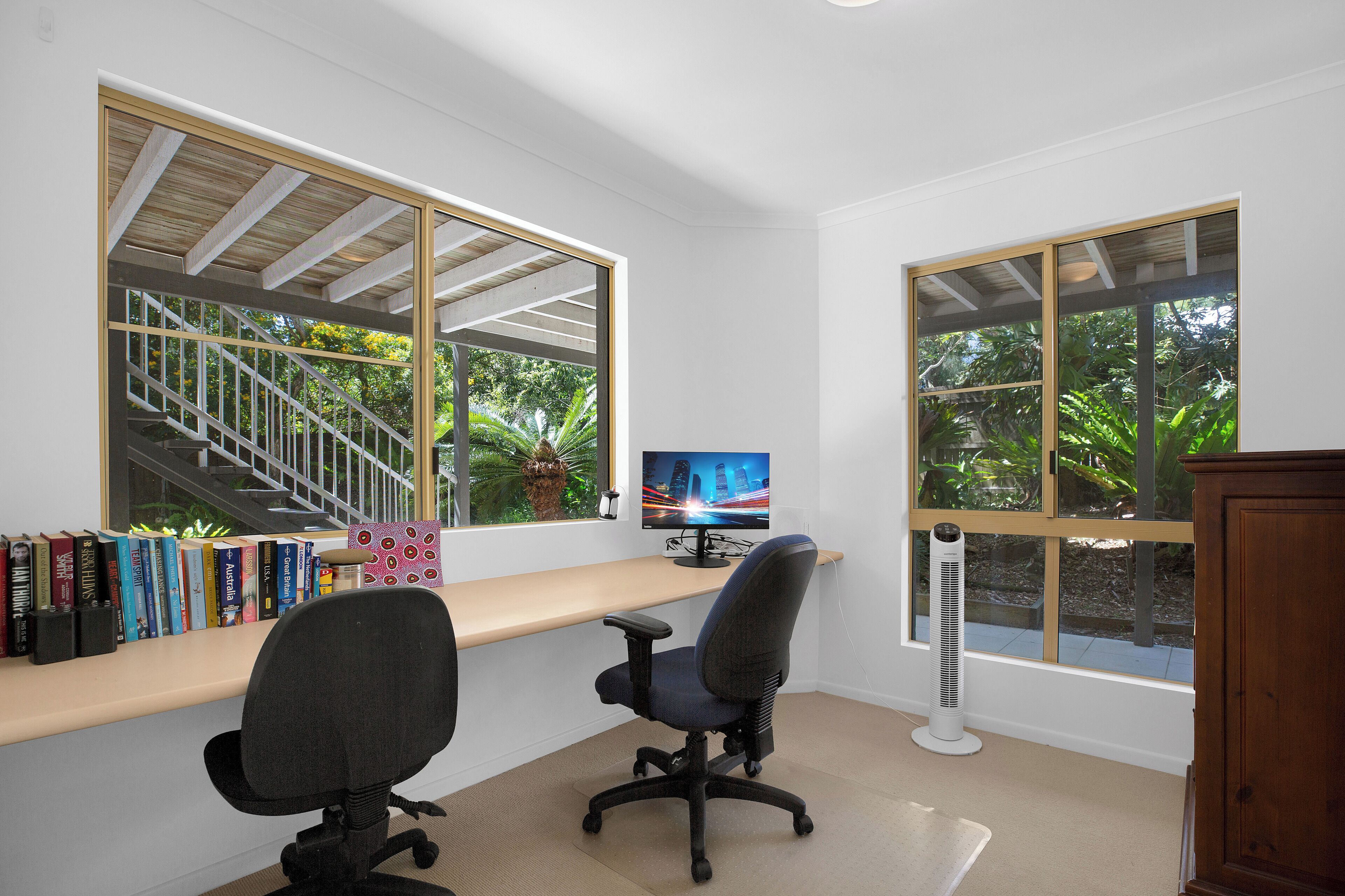 Een werkplek aan huis met een bureau, twee stoelen, een computer en boekenkasten.