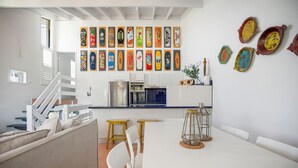 Una cocina moderna con muebles blancos, un comedor con mesa y sillas blancas, y una escalera con barandilla blanca.