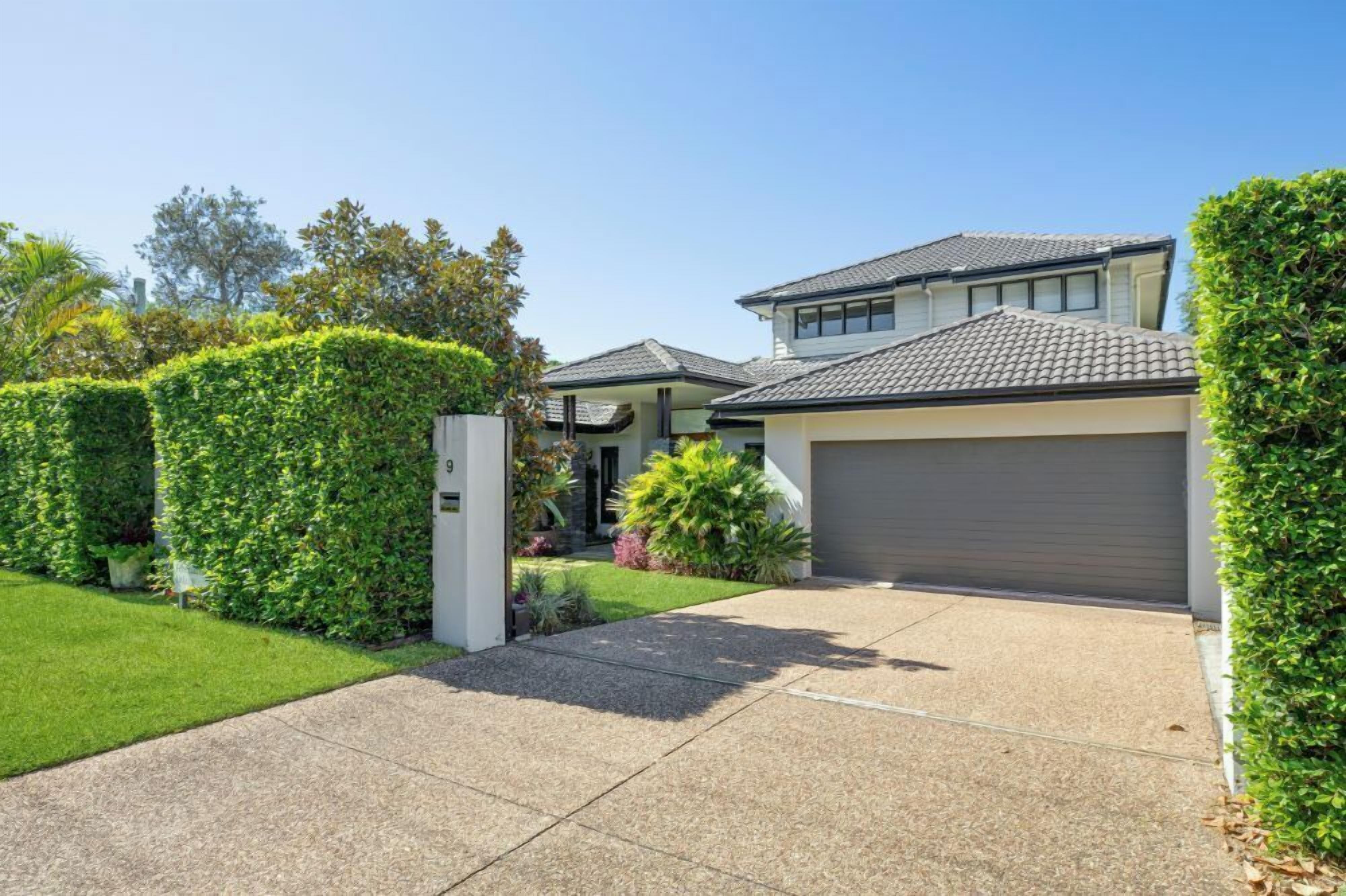 A modern two-story house with a garage, surrounded by well-maintained hedges and a lawn.