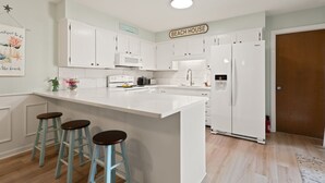 Une cuisine avec des meubles blancs, un grand îlot central doté de tabourets, un four à micro-ondes et un réfrigérateur.