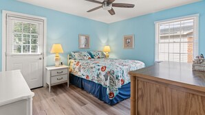 Une chambre à coucher comprenant un lit, des tables de chevet, un ventilateur de plafond et une commode.